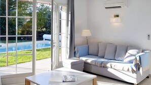 Ein modernes Wohnzimmer mit einem weißen Sofa, einem Couchtisch und Blick auf einen Swimmingpool durch große Glasüren.
