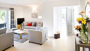 Ein modernes Wohnzimmer mit einer Couch, einem Couchtisch und einem Fernseher. Eine Tür führt zu einem Balkon.
