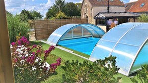 Piscina com duas estruturas envidraçadas, rodeada por um jardim bem cuidado com diversas plantas e flores.