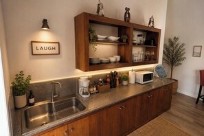 Una cocina moderna con un lavaplatos integrado, armarios de madera, una encimera con diversos electrodomésticos y una repisa con vajilla y una planta en maceta.