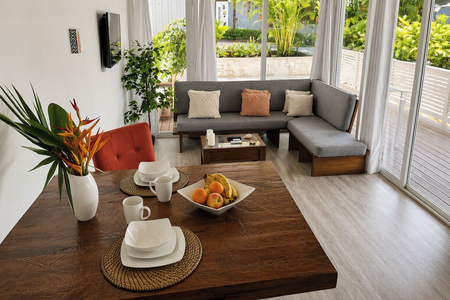 Un salon moderne comprenant un coin repas, un canapé gris agrémenté de coussins, une table basse et une vue sur la verdure à l’extérieur.