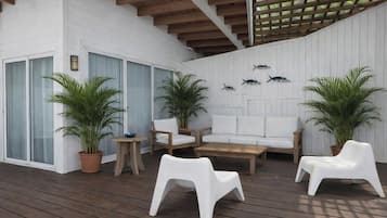 An outdoor patio with a wooden deck, white furniture, and potted plants.