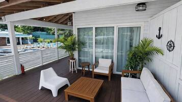 Un espacio exterior cubierto con piso de madera, muebles blancos y plantas en macetas.