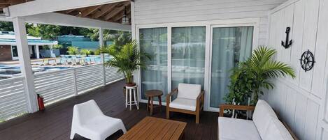 A covered outdoor area with a wooden deck, white furniture, and potted plants.