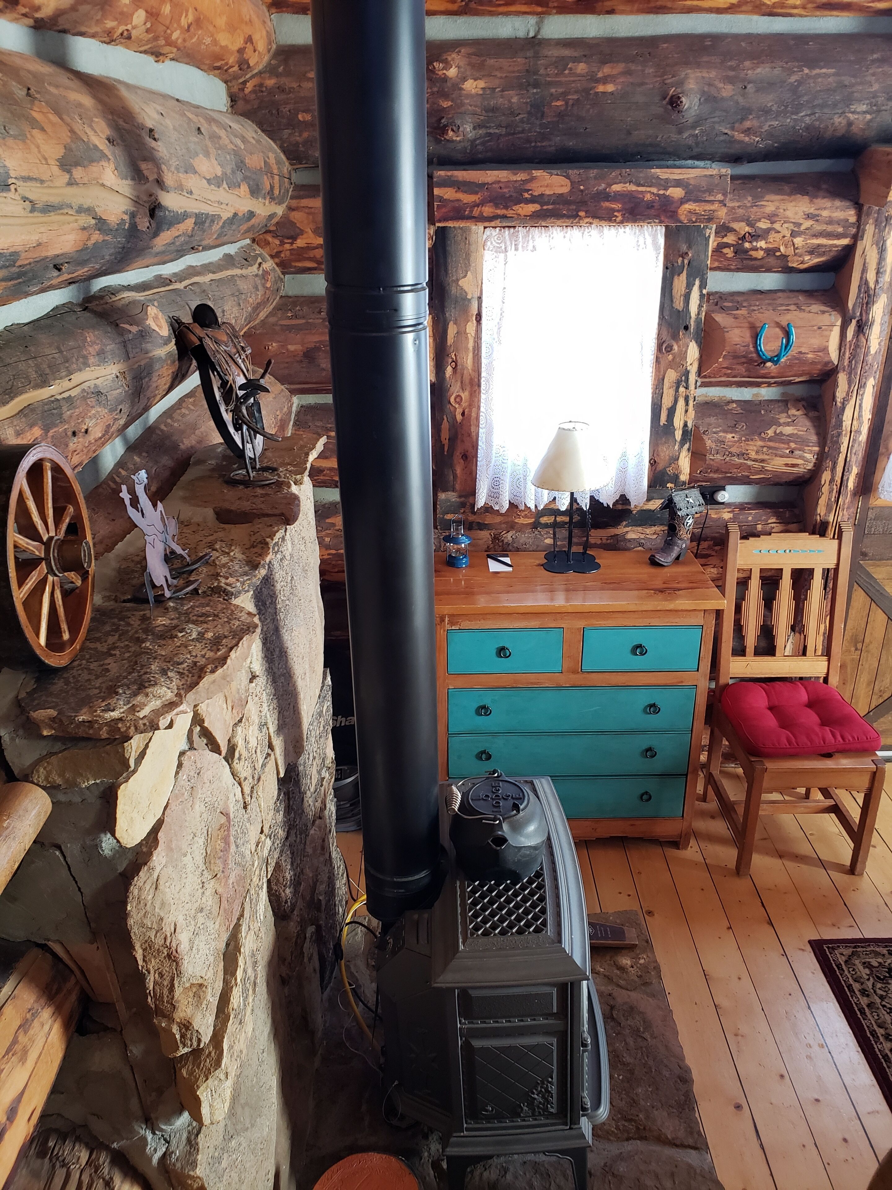 Interior rústico de una cabaña con chimenea de piedra, muebles de madera y una pared de troncos.