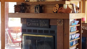 A cozy living room with a fireplace, wooden shelves with books, a clock, and a sign that reads "Friends & Family Gather Here".