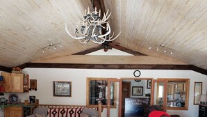 A spacious living area with a leather sofa, a recliner, and a chandelier. There is a kitchen area with wooden cabinets and a dining table.