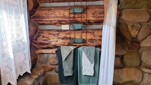 A rustic bathroom with stone walls, a wooden ceiling, and a wicker basket.