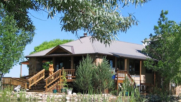 A lodge with a stone exterior, wooden deck, and a pond in front.