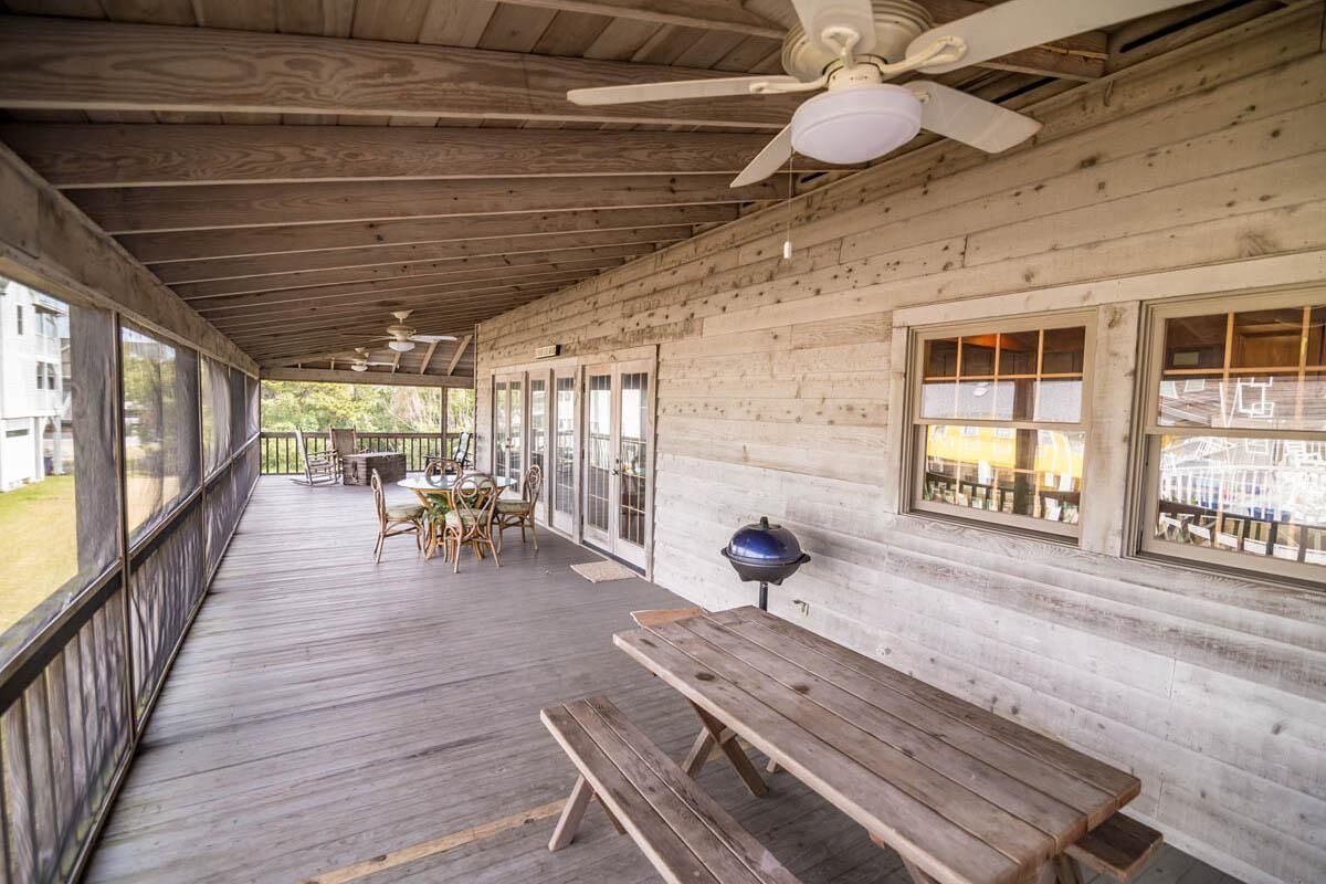 Une terrasse en bois couverte, avec une table et des chaises, un ventilateur de plafond et un barbecue.