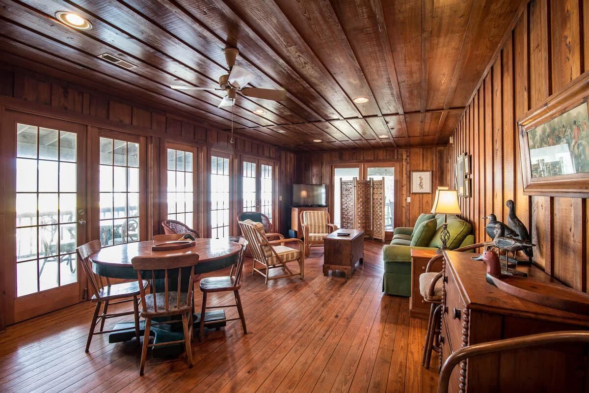 A wooden-floored room with a dining table, chairs, a sofa, and a television.