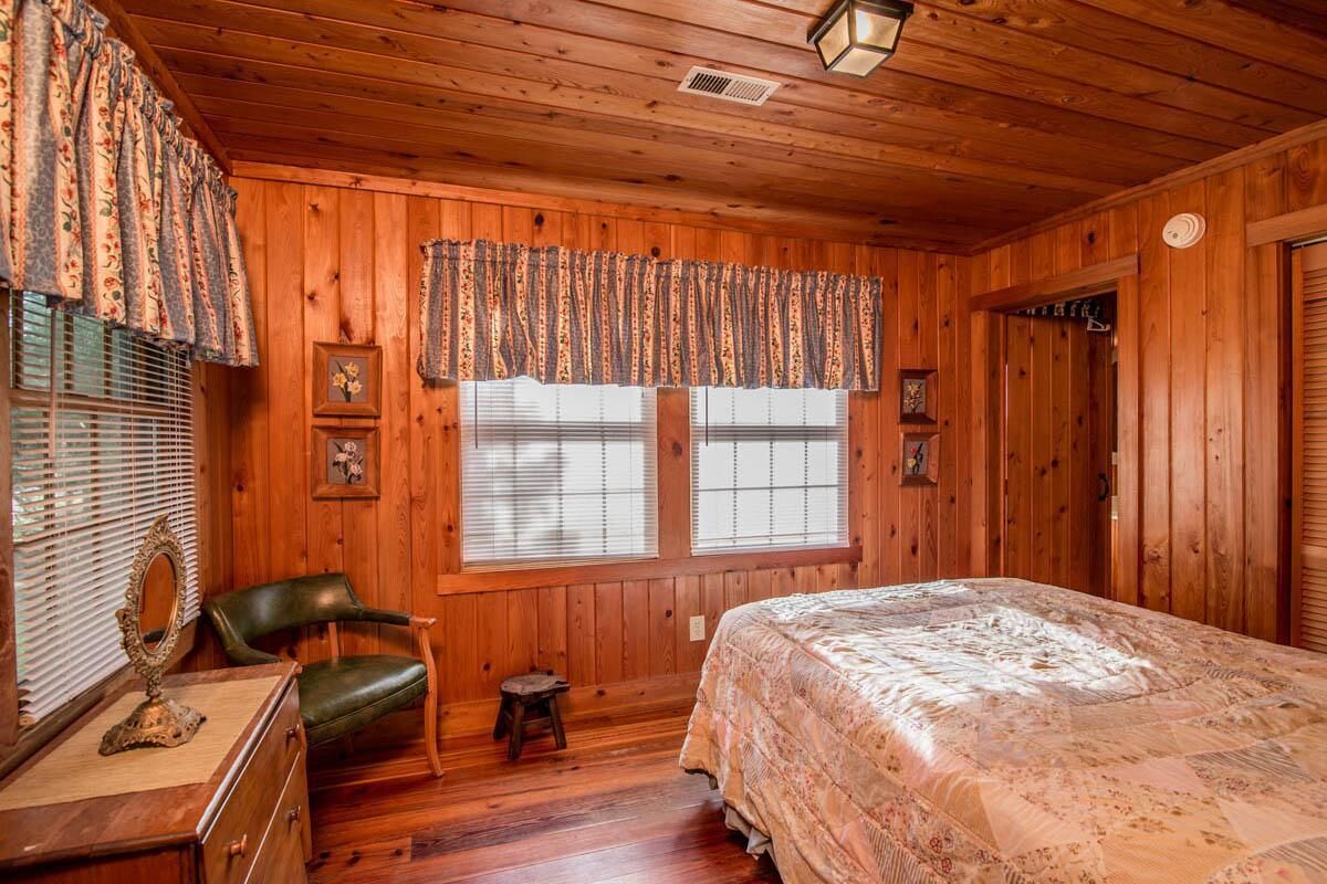 Dormitorio de cabaña de madera con cama, una silla, cómoda y ventana con persianas.