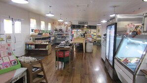 Una panadería con estantes llenos de productos horneados, una exhibición de pan y un refrigerador con pasteles.