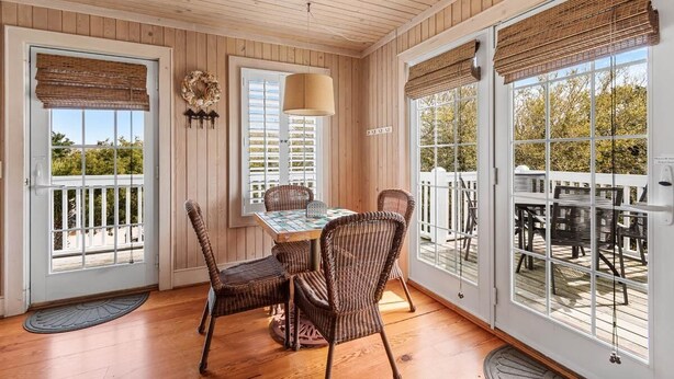 A wooden-paneled room with a dining table and wicker chairs, large windows with blinds, and a view of the outdoors. - CasaUp Charming Duplex in Beautiful Pawleys Island (Pawleys Island)