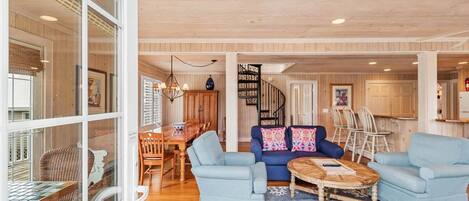 A spacious living room with a blue sofa set, a wooden coffee table, and a dining area with a wooden table and chairs.