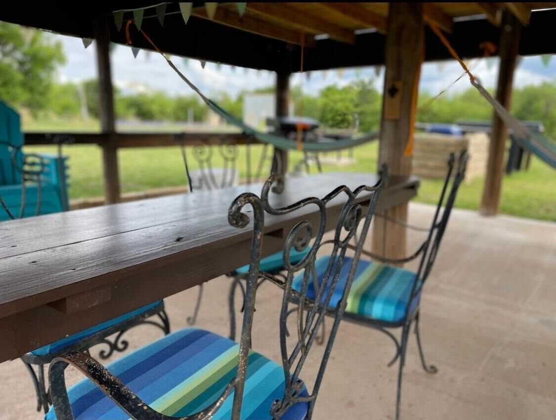 Une terrasse couverte avec une table en bois et des chaises en métal dotées de coussins à rayures.