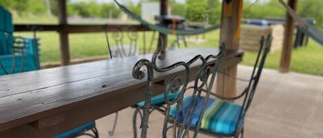 Une terrasse couverte avec une table en bois et des chaises en métal dotées de coussins à rayures.