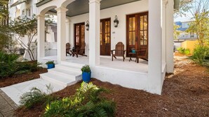 A white building with a covered porch, wooden doors, and steps leading to the entrance. - PRIVATE BEACH/POOL ACCESS-Charming Cottage-Lovely Courtyard-4 Bikes (Panama City Beach)