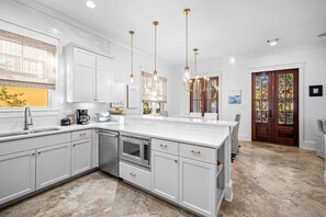 Une cuisine moderne avec des meubles blancs, un grand îlot central, des appareils en acier inoxydable et des luminaires suspendus.