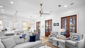 A modern living room with a grey sofa, two armchairs, a coffee table, and a ceiling fan. - PRIVATE BEACH/POOL ACCESS-Charming Cottage-Lovely Courtyard-4 Bikes (Panama City Beach)