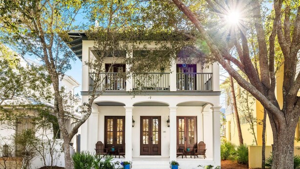 A two-story house with a balcony, white exterior, and a front porch with chairs. - PRIVATE BEACH/POOL ACCESS-Charming Cottage-Lovely Courtyard-4 Bikes (Panama City Beach)