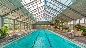 An indoor swimming pool with clear lanes, sunlit by a high ceiling with skylights, surrounded by lounge chairs and potted plants. - PRIVATE BEACH/POOL ACCESS-Charming Cottage-Lovely Courtyard-4 Bikes (Panama City Beach)