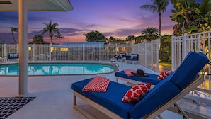 A poolside area with lounge chairs, a pool, and palm trees.