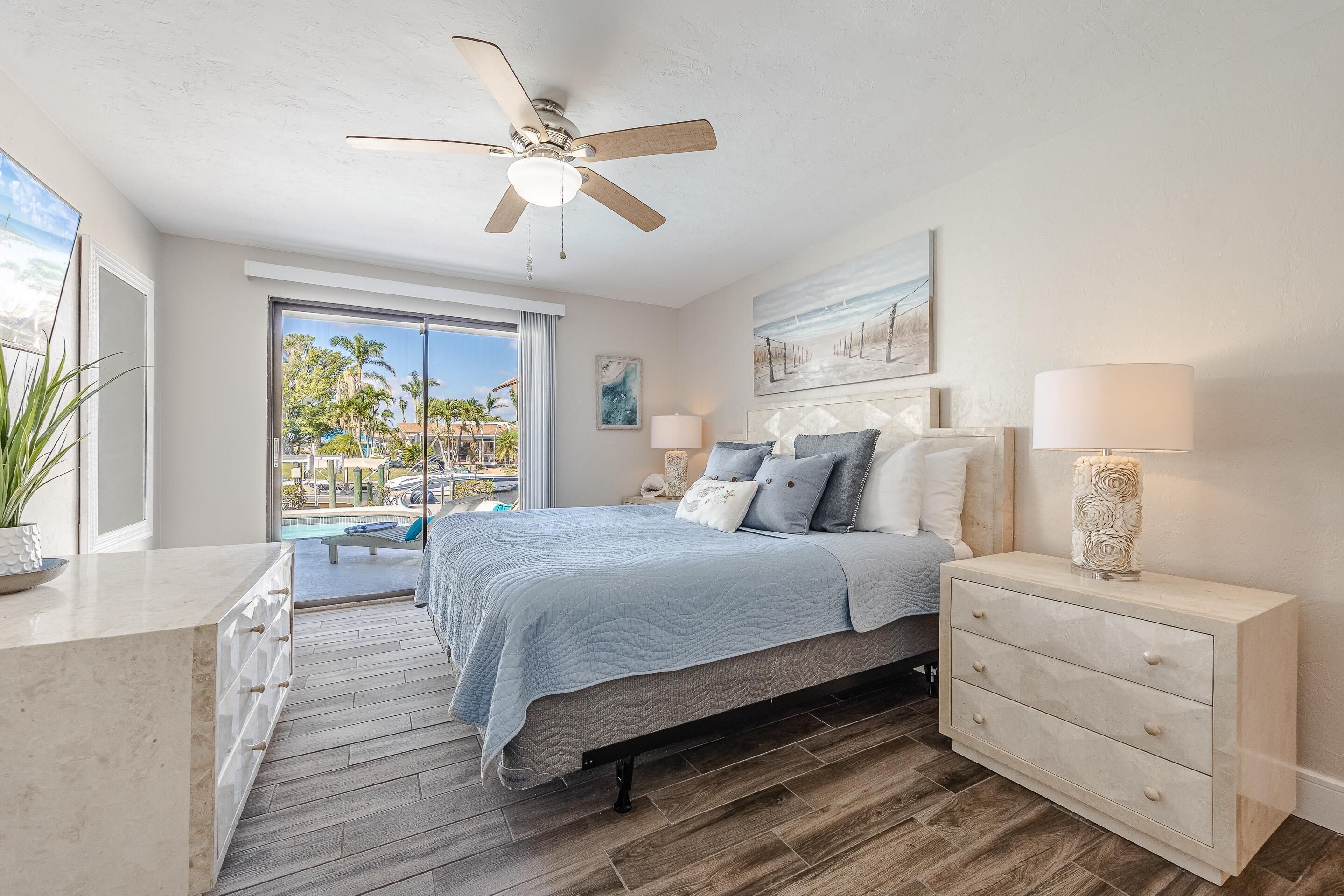 A bedroom with a bed, a nightstand, a dresser, a ceiling fan, and a view of the outdoors.