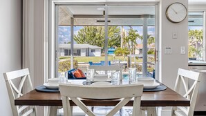 A dining area with a table set for two, a view of the outdoors, and a clock on the wall.