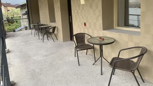 An outdoor patio with tables and chairs, a wooden ceiling, and a view of buildings in the background. - Hotel Lemi (Mestia)