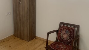 A room with a wooden wardrobe, a chair with a patterned cushion, and a metal wall-mounted shelf. - Hotel Lemi (Mestia)