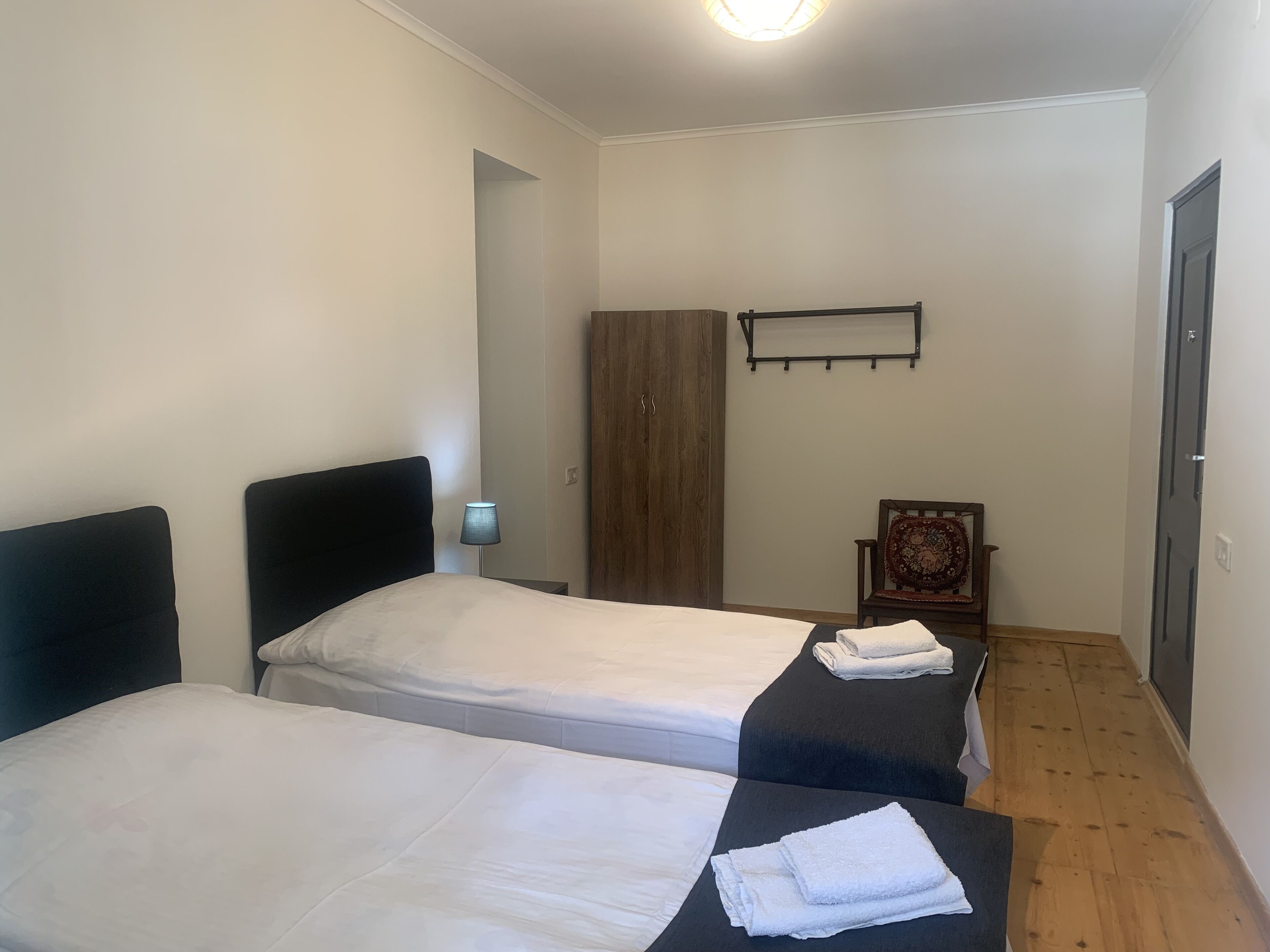 Una habitación con dos camas, un armario de madera, una silla y un estante en la pared.