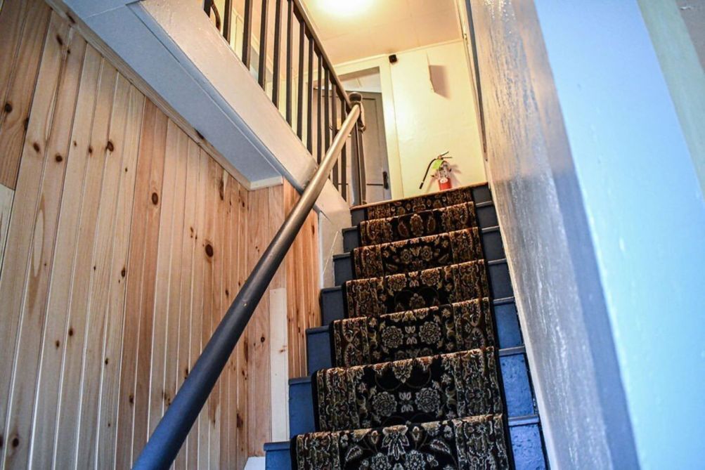 A wooden staircase with a metal handrail and patterned carpet.
