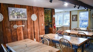 A rustic dining area with wooden tables and chairs, a painting of flowers, and a forest mural. - Red,White & Blue/Brook Road Inn (Goshen)
