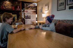Dos personas sentadas en una mesa de madera en una habitación con pared de piedra y cuadros.