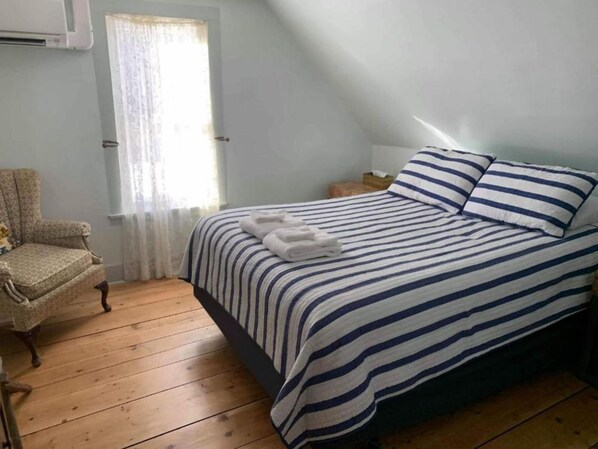 Un dormitorio con cama, una silla, un ventanal y una mesita de noche.
