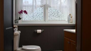 Ein Badezimmer mit Toilette, einem Fenster mit Spitzenvorhang, einem Heizkörper und einem Holzschrank.