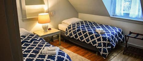 A small, cozy room with two beds, a nightstand, a lamp, and a window.