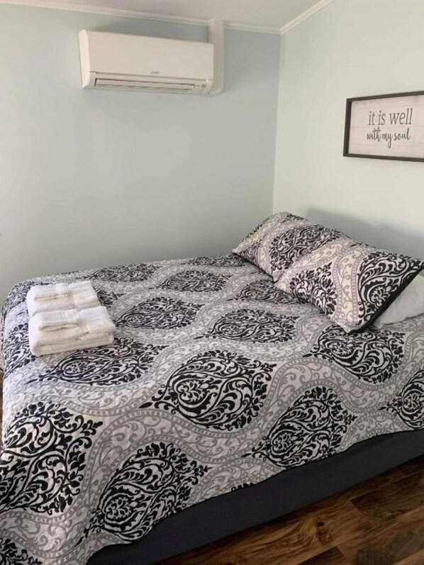 A bedroom with a patterned bedspread, a neatly folded towel, and a motivational quote on the wall.