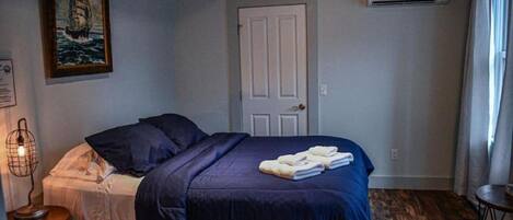 A bedroom with a bed, a door, an air conditioning unit, and a painting on the wall.