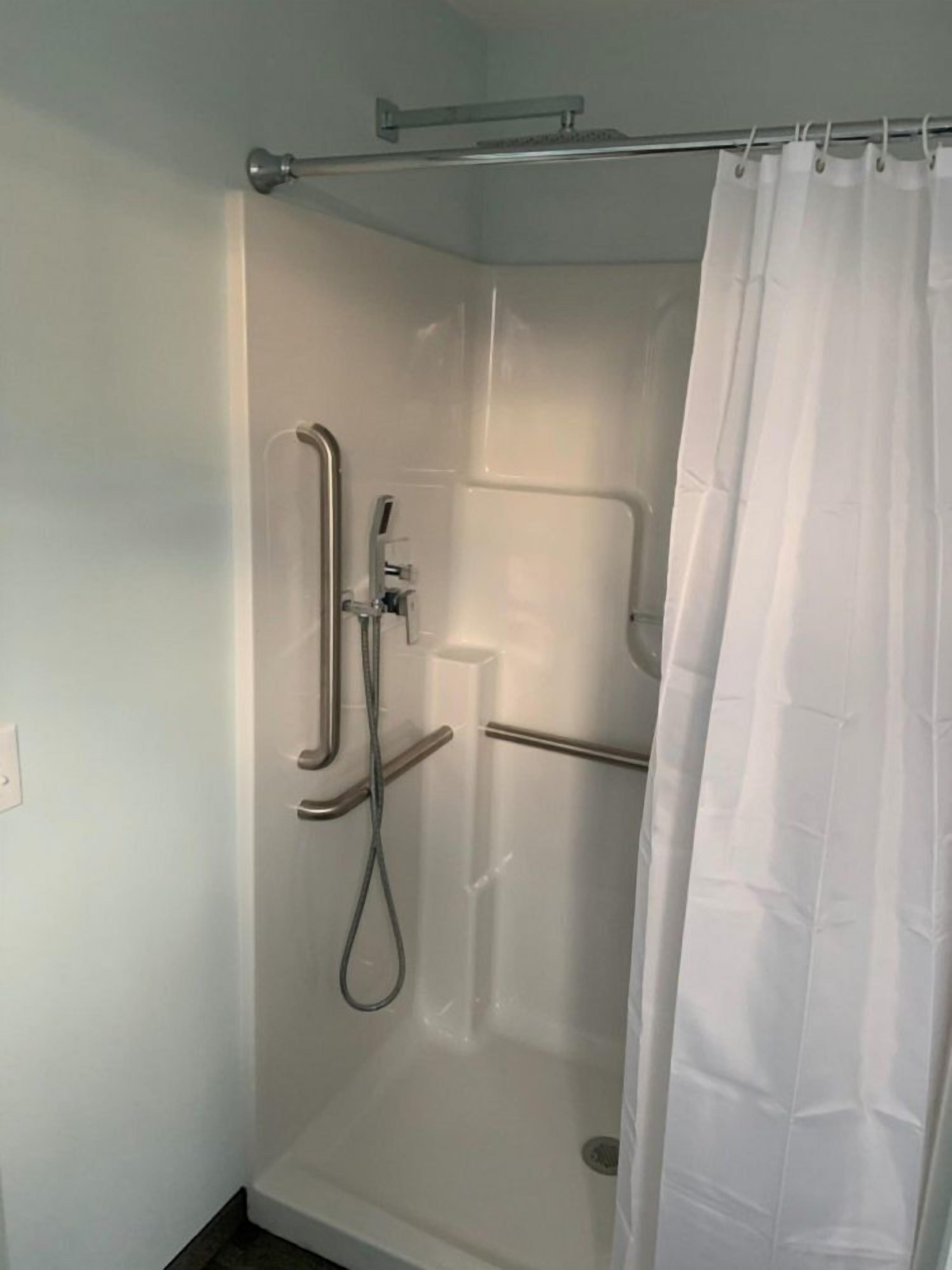 A walk-in shower with a glass door, a handheld showerhead, and a grab bar.