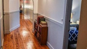 A narrow hallway with wooden flooring, white walls, and a bookshelf.