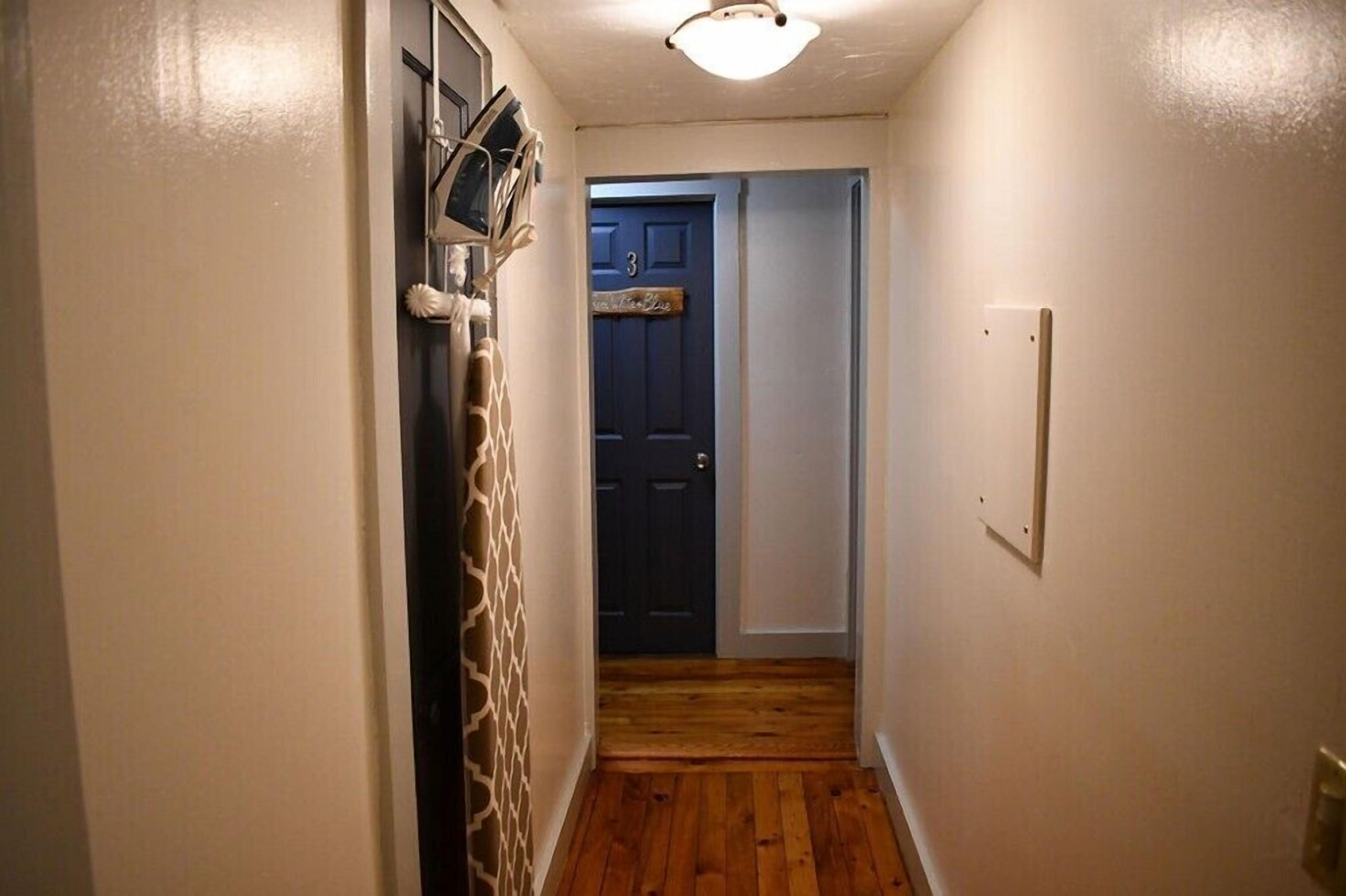 A narrow hallway with wooden flooring, a dark blue door, and a light switch on the wall.