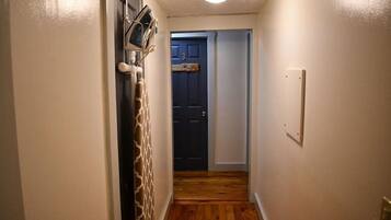A narrow hallway with wooden flooring, a dark blue door, and a light switch on the wall.