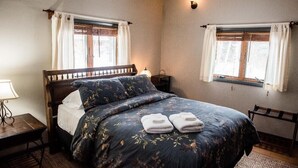 A bedroom with a wooden bed, two bedside tables, a nightstand, and a window with curtains. - Brook Road Cabin (Goshen)