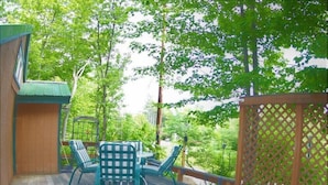 A wooden deck with a table and chairs, surrounded by a wooden fence and trees. - Brook Road Cabin (Goshen)