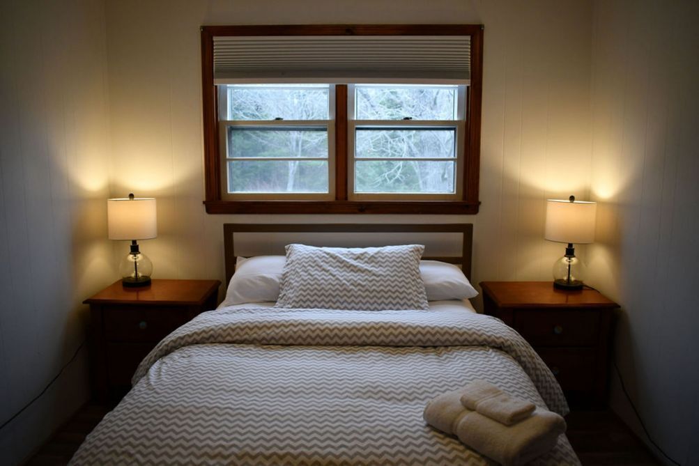 Une chambre à coucher avec un lit, deux lampes de chevet, une fenêtre et une tête de lit en bois.