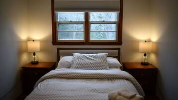 Une chambre à coucher avec un lit, deux lampes de chevet, une fenêtre et une tête de lit en bois.