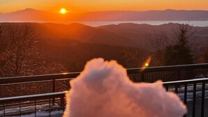 Une vue sur le coucher de soleil depuis un balcon doté d’une balustrade, donnant sur une vallée et des montagnes lointaines.