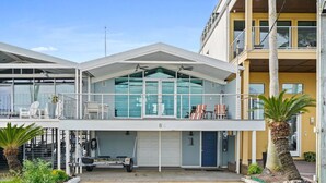 A two-story building with a covered balcony, a garage, and a small outdoor seating area with chairs and a table.
